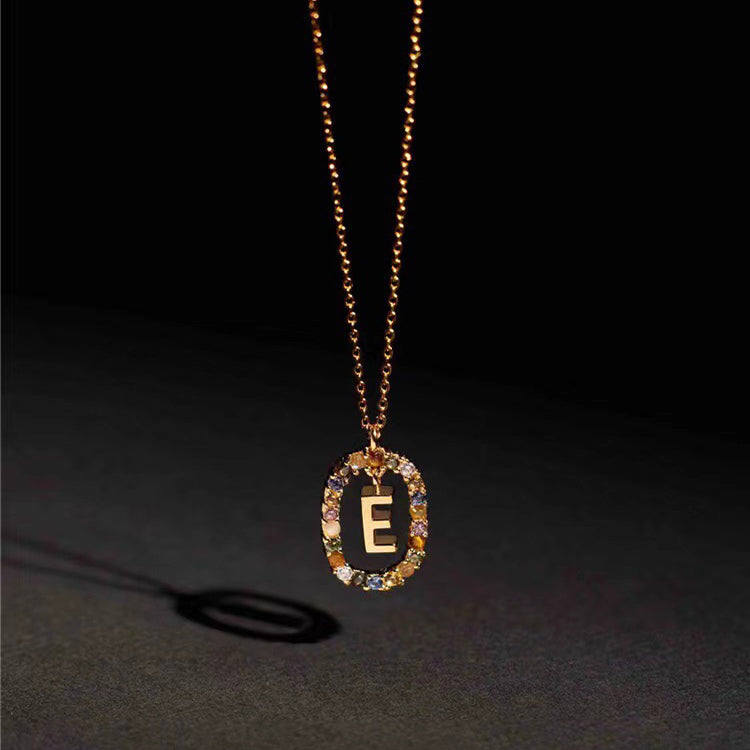 Gold necklace with a pendant featuring the letter 'E' on a dark background