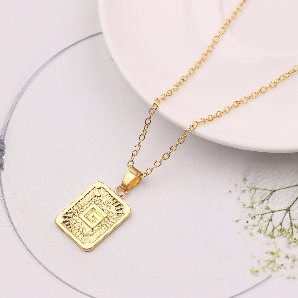 Gold necklace with a square pendant on a white surface with flowers