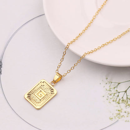 Gold necklace with a square pendant on a white surface with flowers