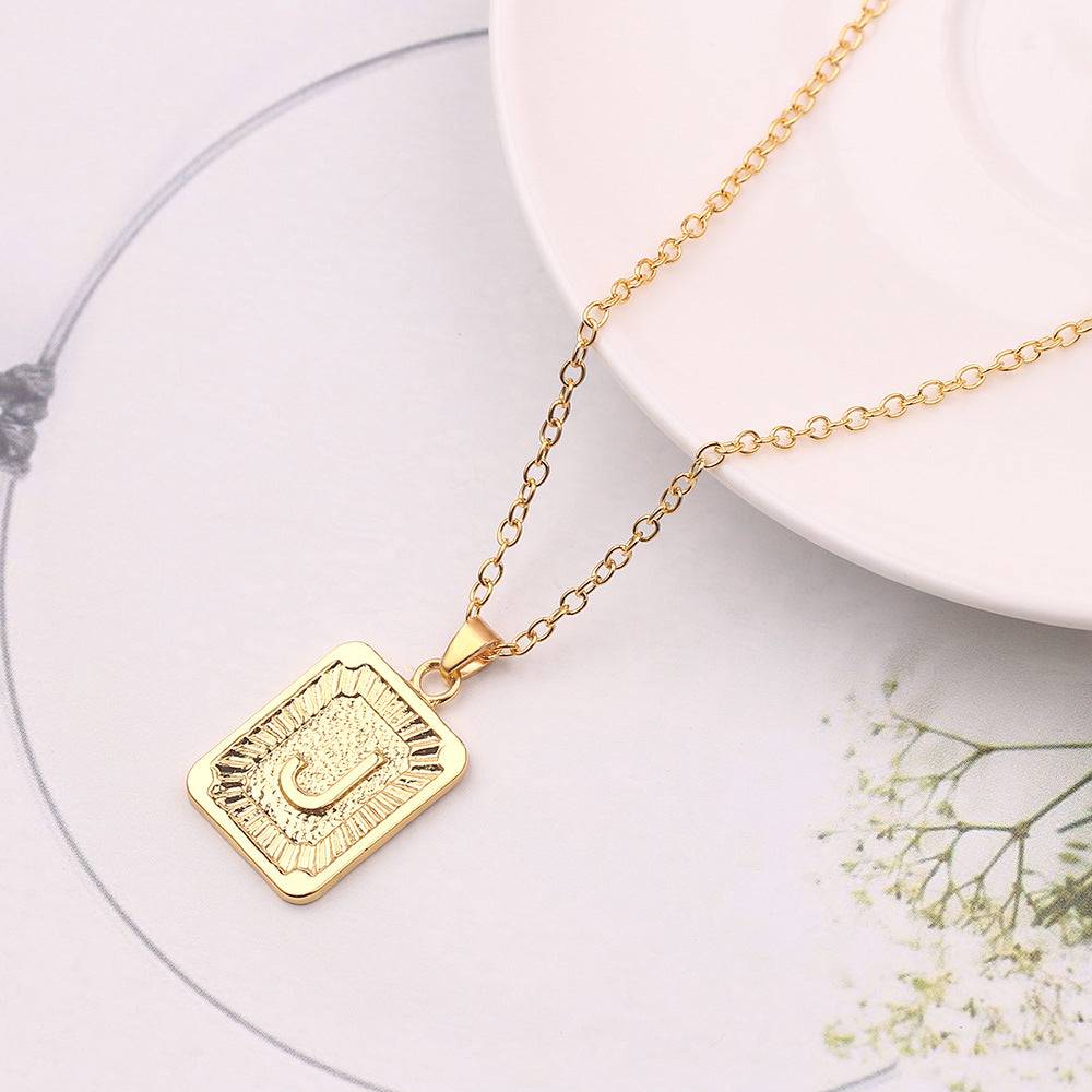 Gold necklace with a square pendant on a white surface with small flowers.