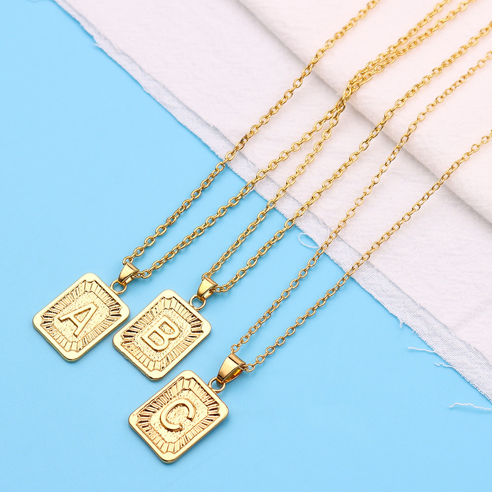 Gold necklaces with square pendants on a blue and white fabric background